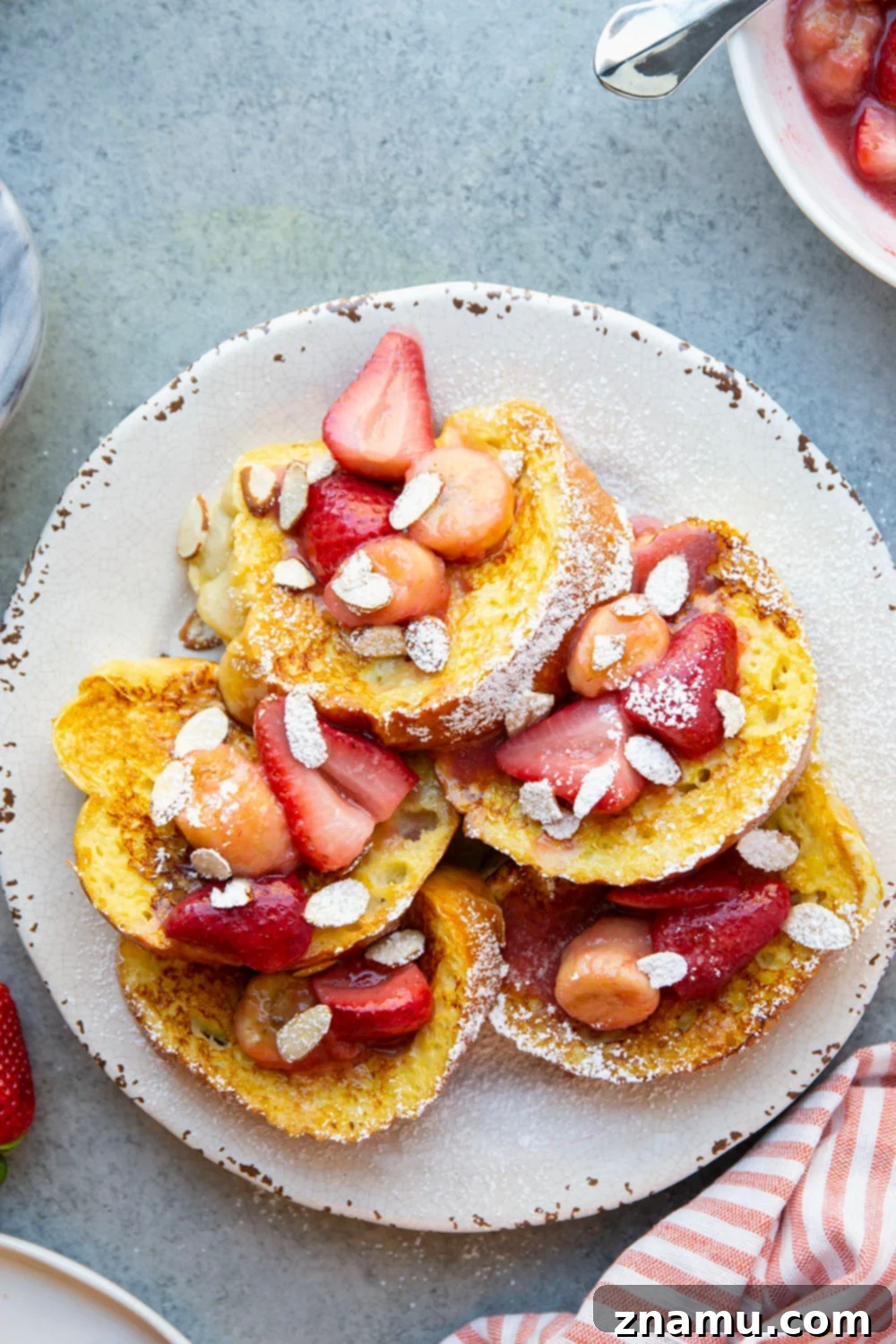 Amaretto French Toast: Caramelized Strawberry Banana Delight 3 Close-up of golden Amaretto French Toast slices drizzled with caramelized strawberry banana sauce and powdered sugar.