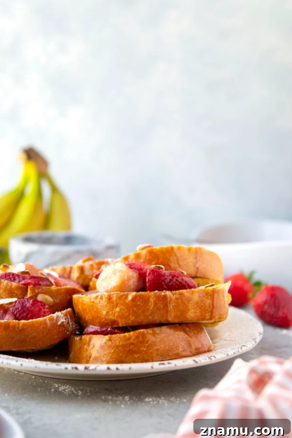 Amaretto French Toast: Caramelized Strawberry Banana Delight 4 Individual serving of Amaretto French Toast with a generous dollop of strawberry banana sauce and toasted almonds.