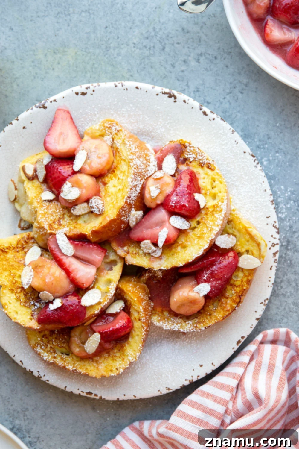 Amaretto French Toast: Caramelized Strawberry Banana Delight 6 Stack of golden French toast slices, topped with fruit sauce and powdered sugar, ready to serve.