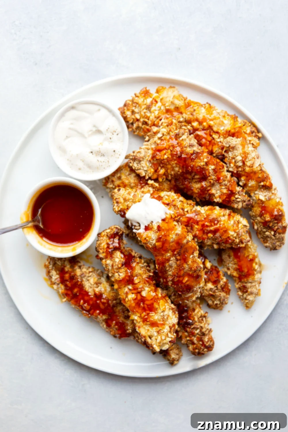 Air Fryer Crispy Pretzel Chicken with Hot Honey Glaze 6 A hand drizzling hot honey glaze over air fryer pretzel crusted chicken tenders, with a bowl of ranch dressing in the background.