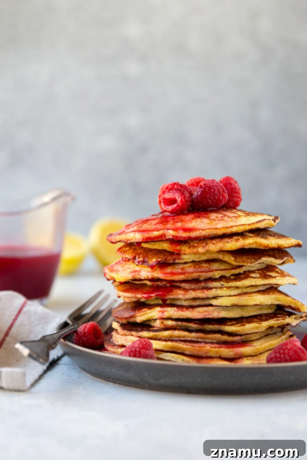 Fluffy Lemon Cottage Cheese Pancakes with Raspberry Drizzle 2 A tall stack of incredibly soft and airy lemon cottage cheese pancakes, generously drizzled with a vibrant homemade raspberry syrup and garnished with fresh raspberries. The golden-brown pancakes have a fluffy texture, suggesting a delightful breakfast experience. Only a handful of ingredients needed and they're naturally gluten-free.