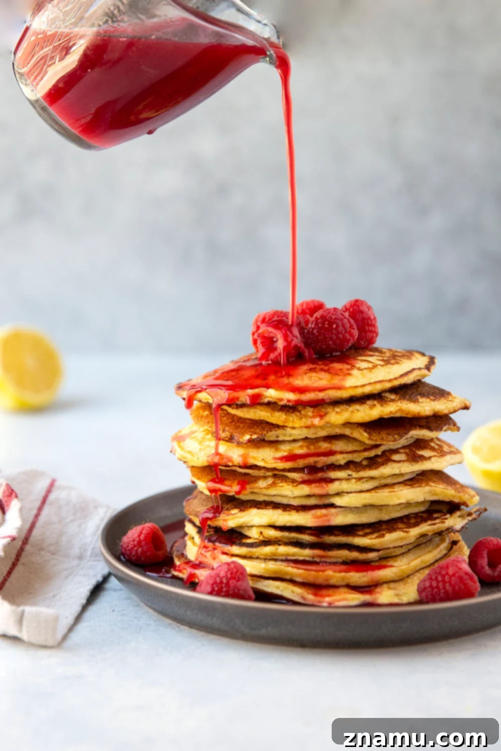 Fluffy Lemon Cottage Cheese Pancakes with Raspberry Drizzle 4 A vibrant close-up of a glass bowl filled with fresh, bright red raspberries, highlighted by sunlight. This ingredient is central to the tangy homemade raspberry syrup that accompanies the fluffy lemon cottage cheese pancakes. The image suggests freshness and natural goodness, emphasizing the wholesome components of this gluten-free recipe.