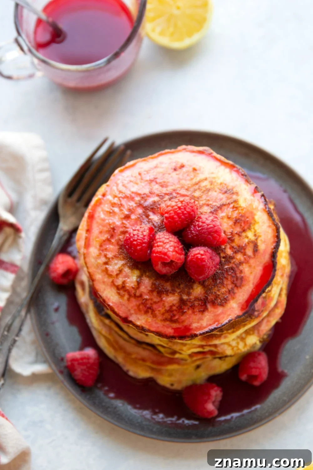 Fluffy Lemon Cottage Cheese Pancakes with Raspberry Drizzle 5 A close-up of a single golden-brown lemon cottage cheese pancake with a dollop of creamy white cottage cheese and fresh raspberries on top, ready to be served. The focus is on the textured, soft pancake, emphasizing the key ingredients and highlighting its light, airy quality. This naturally gluten-free and protein-rich breakfast is a delightful and healthy choice.