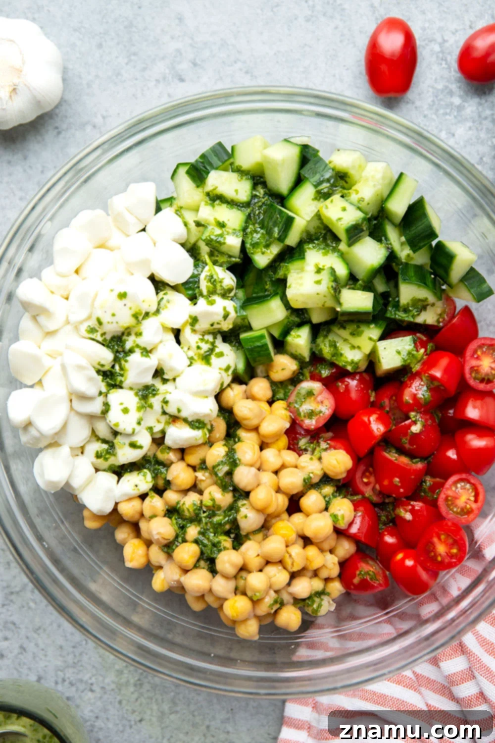 Roasted Garlic Basil Caprese Chickpea Salad 3 Close-up shot of Caprese Chickpea Salad in a rustic bowl, showcasing the fresh ingredients: halved cherry tomatoes, cubed cucumber, white mozzarella pearls, and light brown chickpeas, all glistening with the herbaceous dressing.