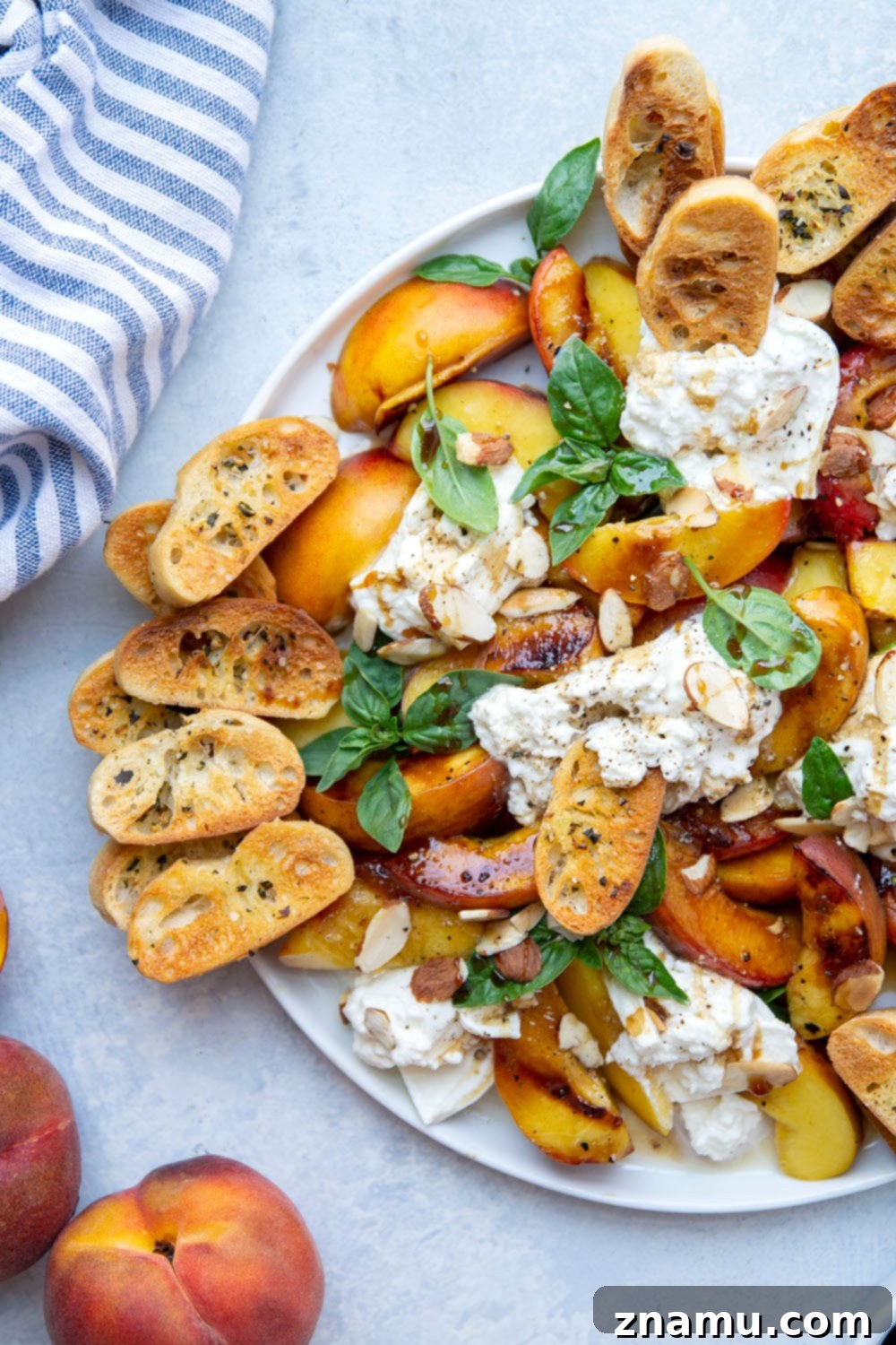 Smoky Grilled Peaches with Creamy Burrata 3 Close-up of grilled peaches and burrata with fresh basil and crostini on a serving platter.