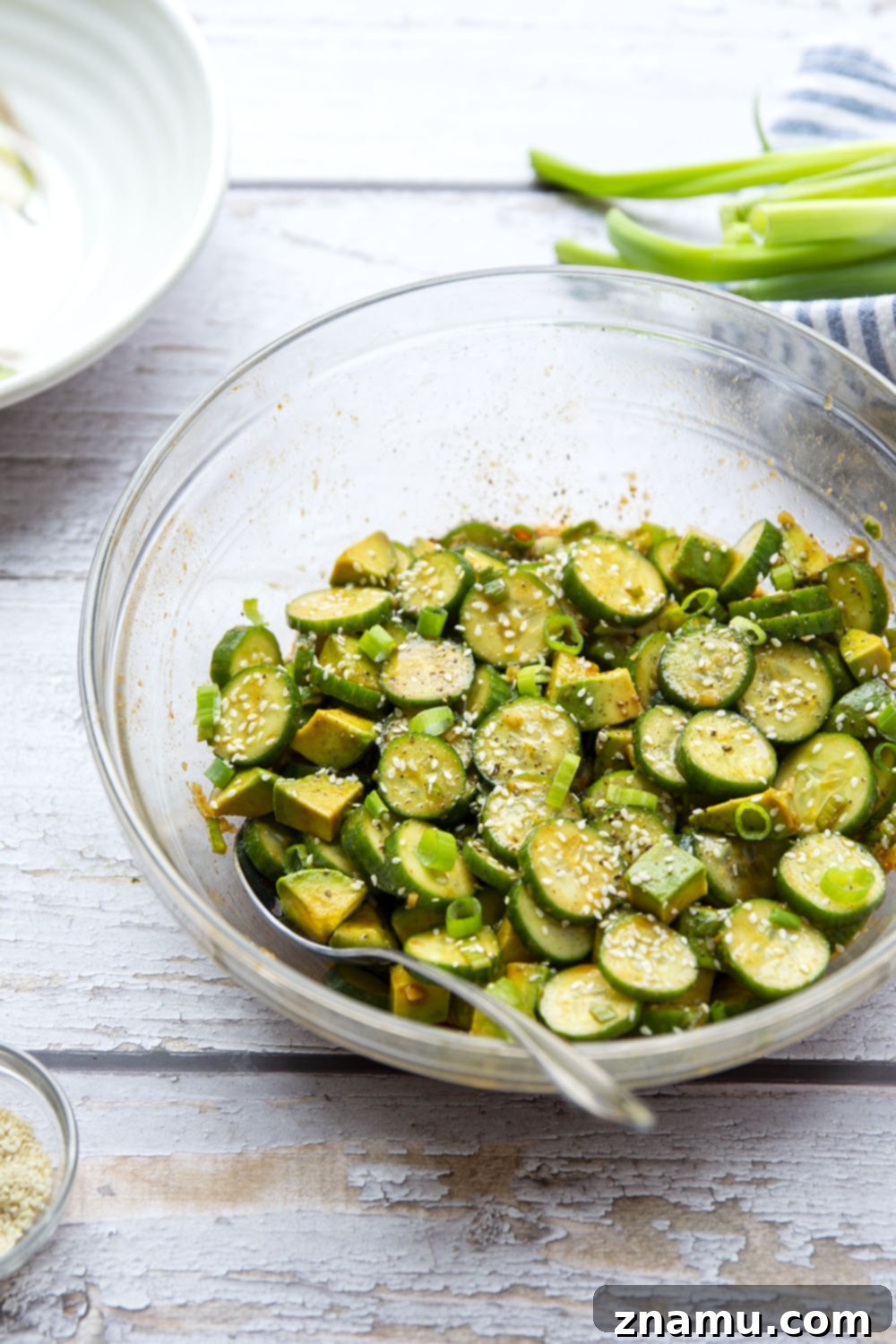 Vibrant Asian Cucumber Avocado Medley 6 A large bowl of finished Asian Cucumber Avocado Salad, garnished with sesame seeds and green onions, ready for serving.