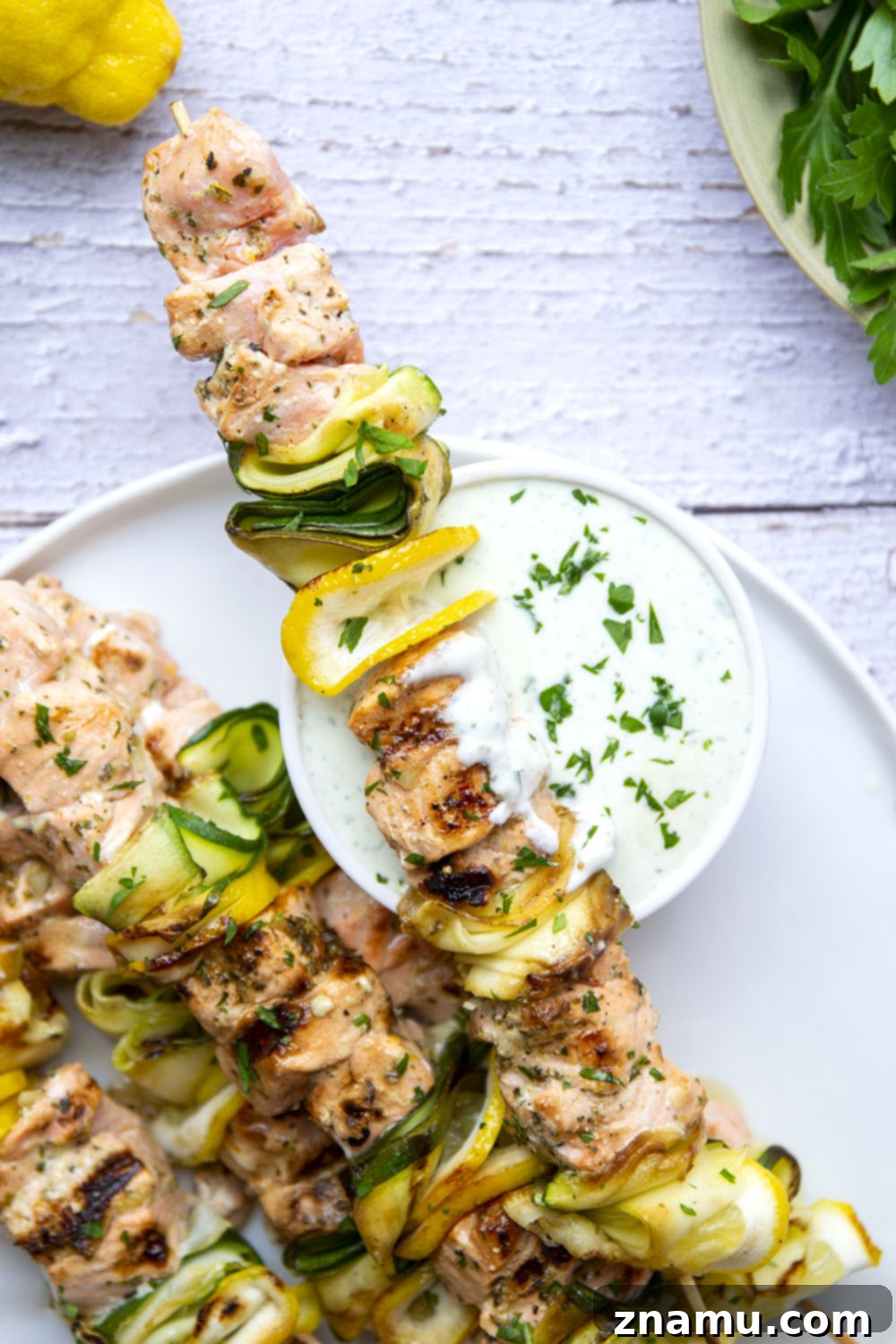 Mediterranean Salmon Skewers with Whipped Feta 6 A serving of Greek grilled salmon and zucchini kabobs on a plate, with a spoon of feta sauce ready for dipping.