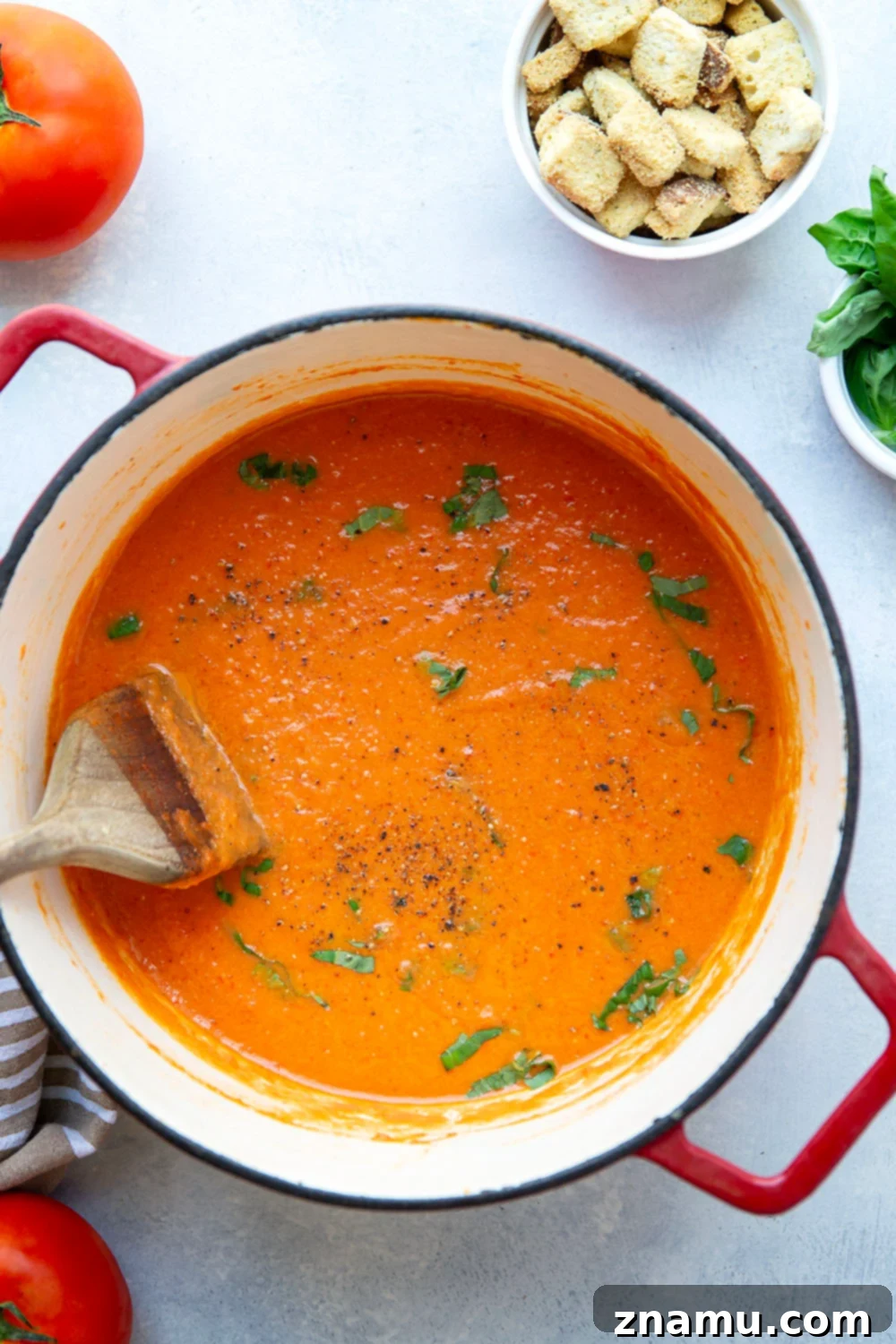 Crimson Fire-Roasted Tomato & Pepper Bisque 6 A beautifully presented bowl of creamy roasted red pepper tomato soup, with a spoon ready for tasting, suggesting a comforting meal.