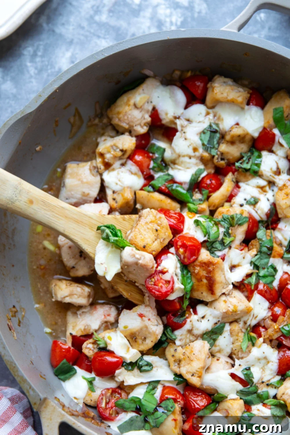 Caprese Chicken Skillet 5 Close-up of raw boneless, skinless chicken breasts on a cutting board, prepped for cubing, alongside fresh cherry tomatoes and basil, emphasizing the quality of ingredients before cooking.