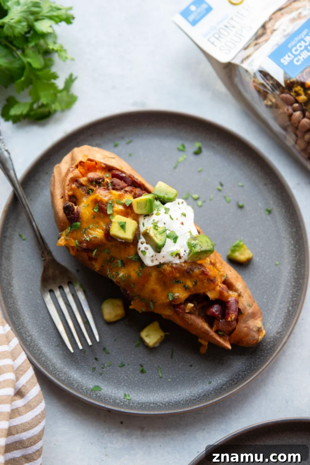 Ultimate Cheesy Chili Sweet Potatoes 5 A table spread with various toppings for chili stuffed sweet potatoes including cilantro, avocado, sour cream, and fresh jalapenos.