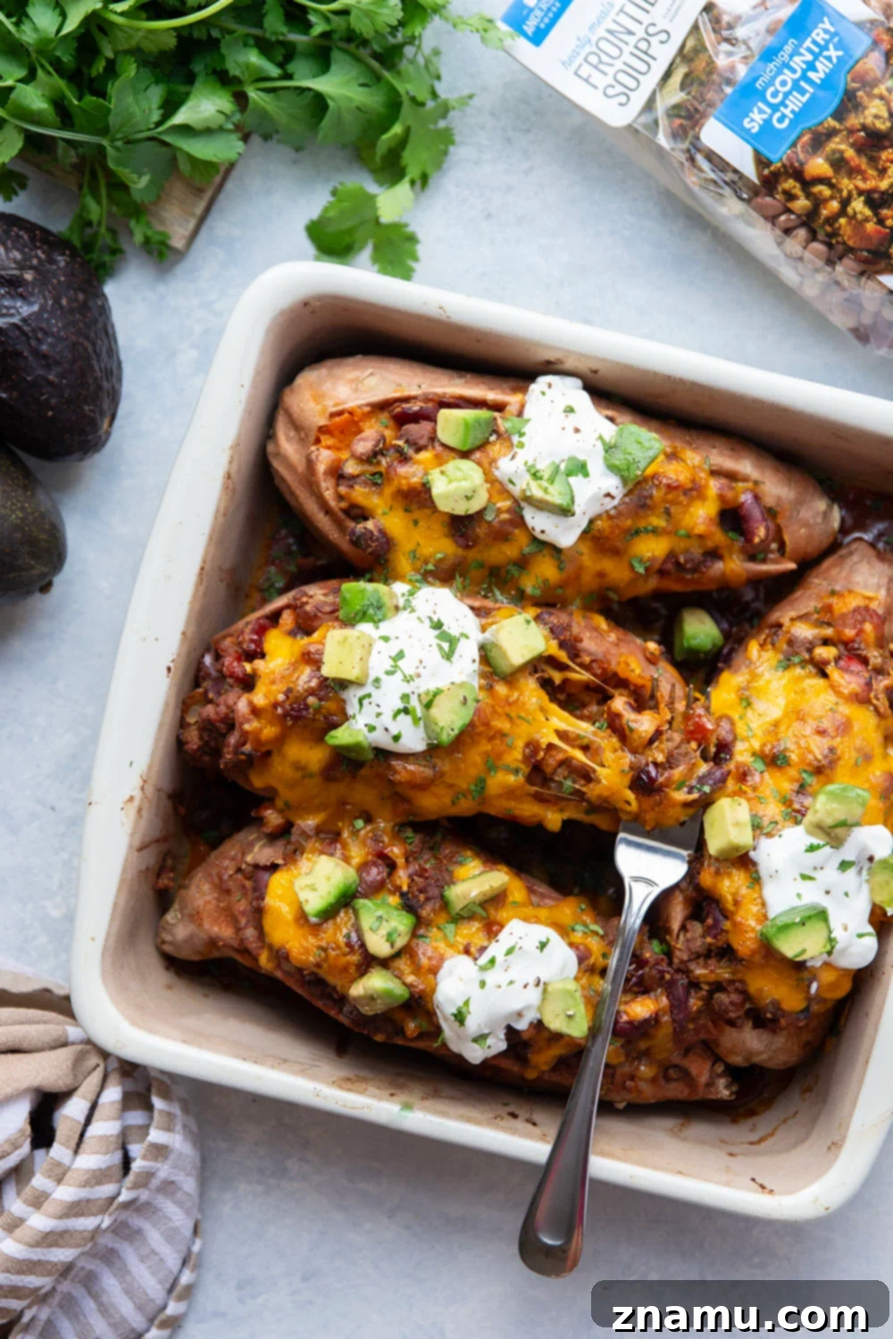 Ultimate Cheesy Chili Sweet Potatoes 6 Overhead shot of two chili stuffed sweet potatoes, richly topped with melted cheese, fresh cilantro, and sour cream.