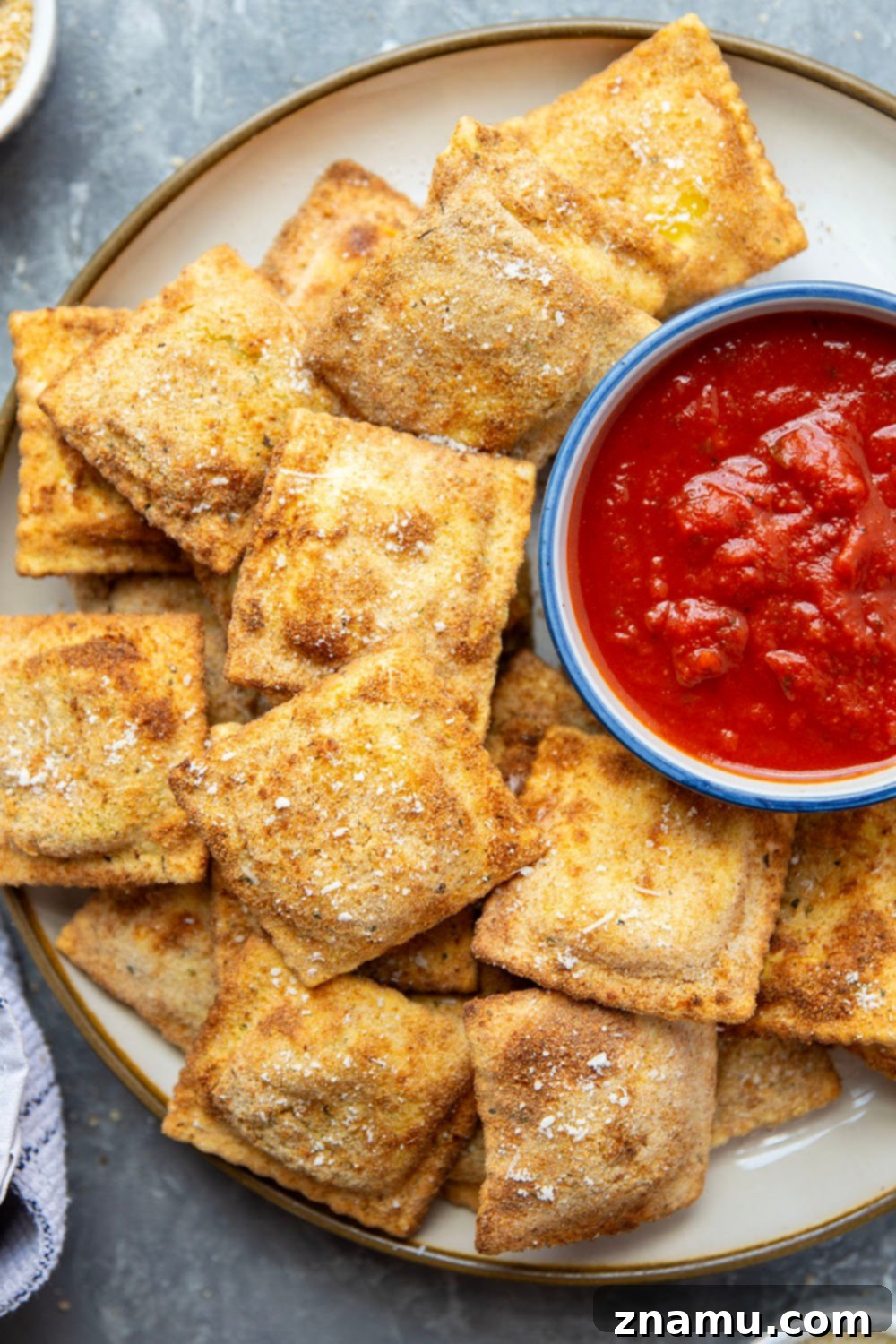 Crispy Air Fryer Ravioli 4 Ingredients for Air Fryer Toasted Ravioli laid out on a white surface, including ravioli, breadcrumbs, eggs, and spices.