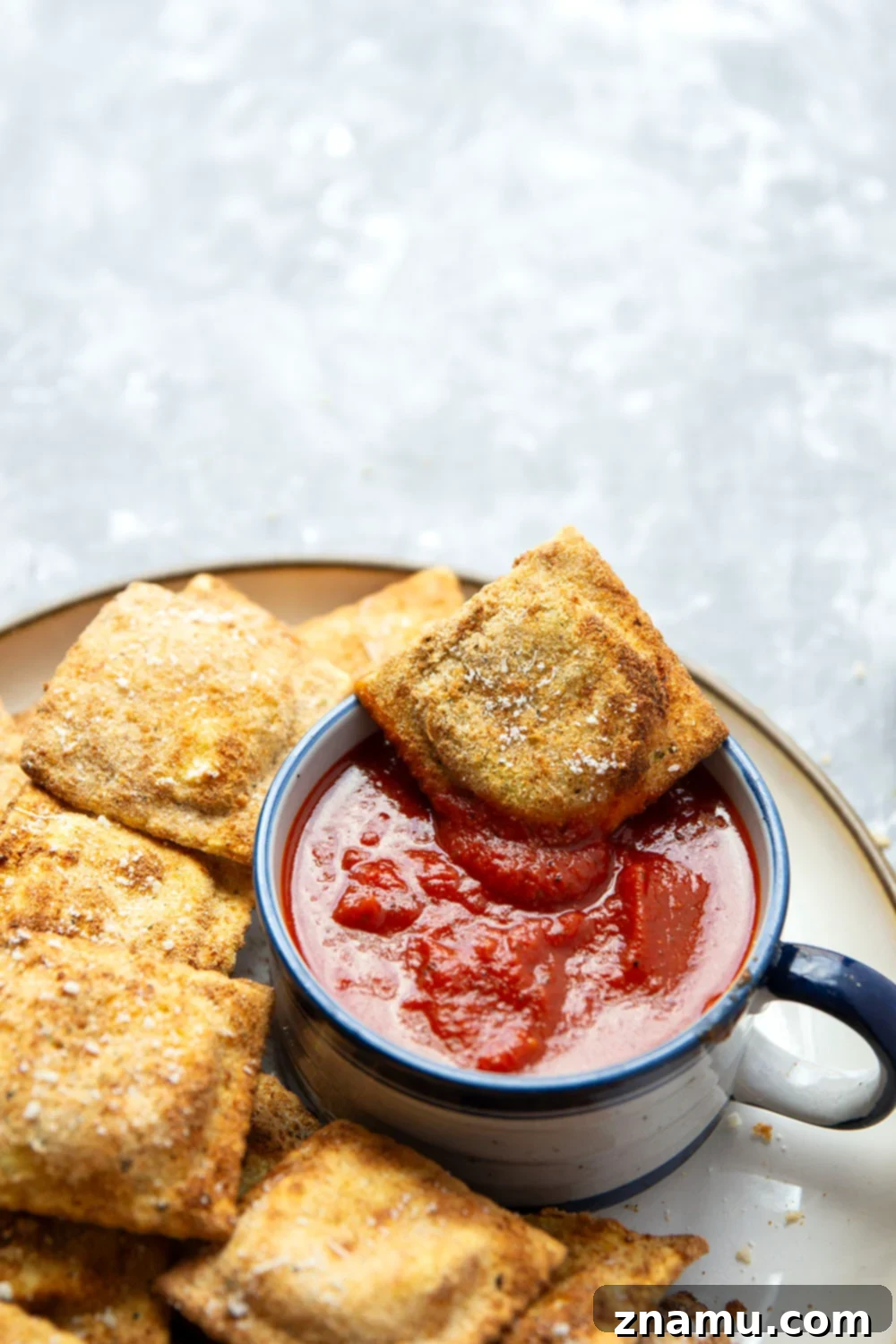 Crispy Air Fryer Ravioli 6 A serving of Air Fryer Toasted Ravioli on a dark plate, ready to be enjoyed.