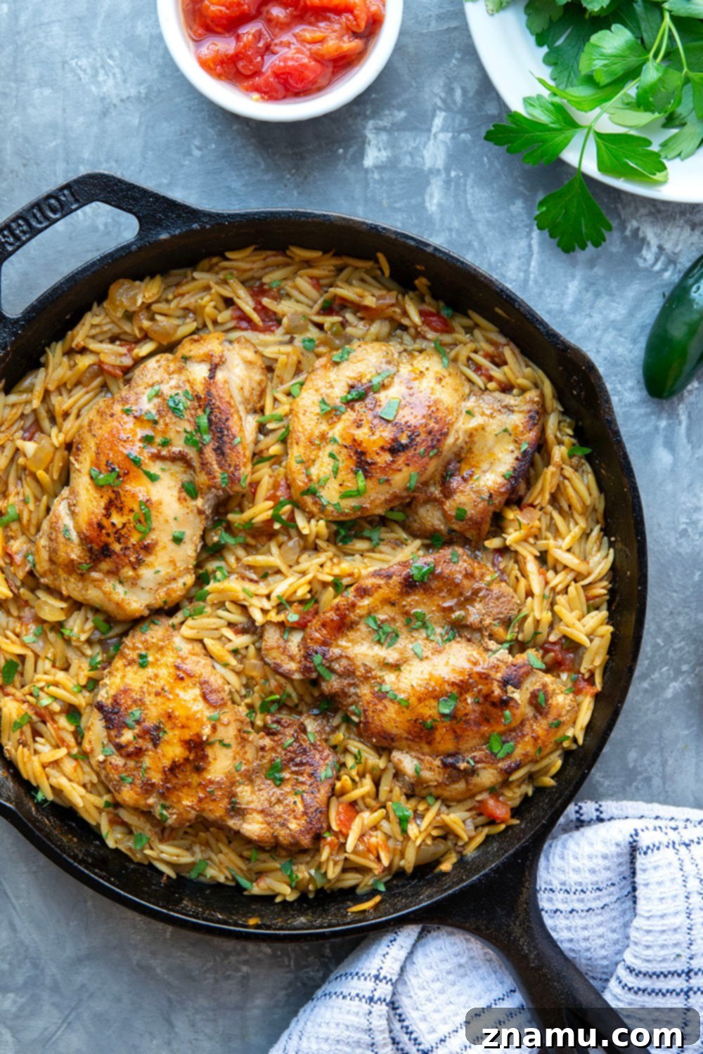 A cast iron skillet with seared chicken thighs and creamy orzo, ready to be served. Fresh parsley is sprinkled on top. The setting is warm and inviting.