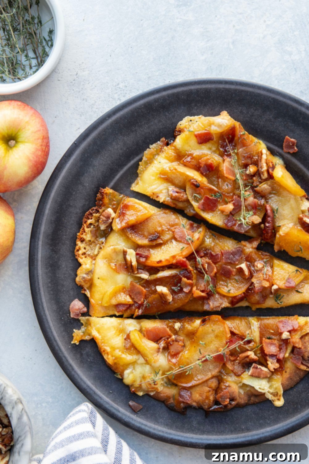 Gourmet Caramelized Apple Brie Flatbread 4 Ingredients for caramelized apple brie flatbread laid out on a counter, including apples, brie, bacon, and naan.