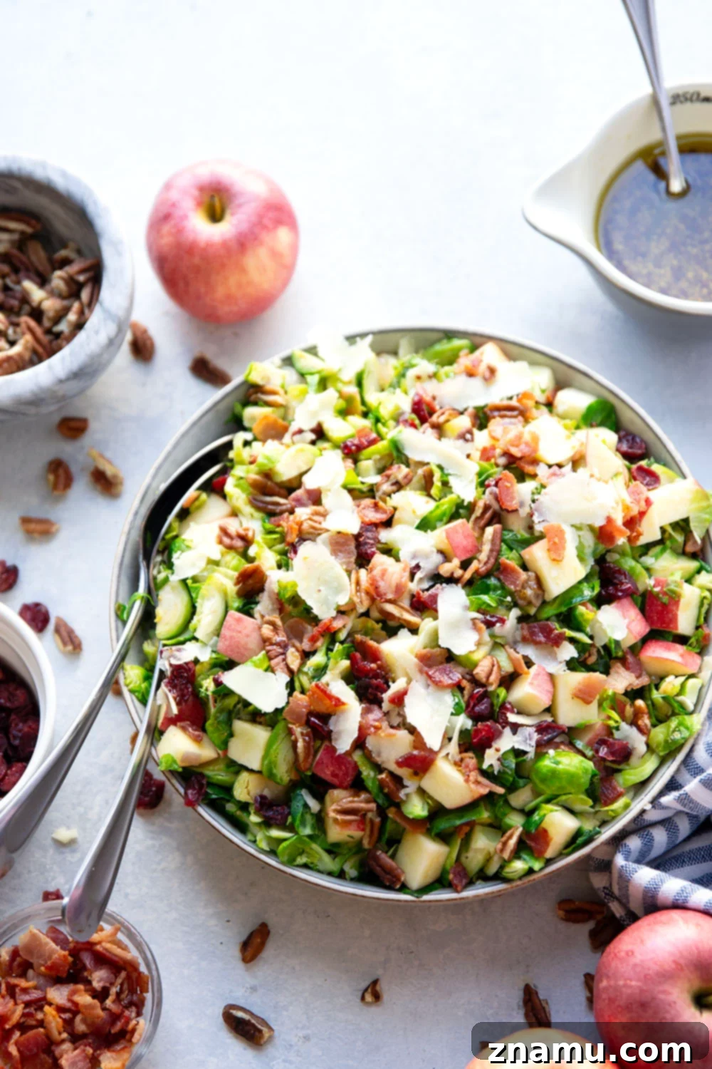 A beautifully plated warm Brussels sprouts salad featuring tender sautéed Brussels sprouts, crispy bacon bits, crunchy apple pieces, and toasted pecans, all coated in a maple mustard dressing, garnished with shaved Parmesan cheese.