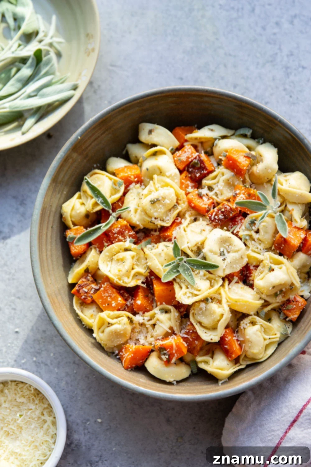 A close-up shot of sage roasted butternut squash and tortellini coated in browned butter garlic sauce, served in a skillet.