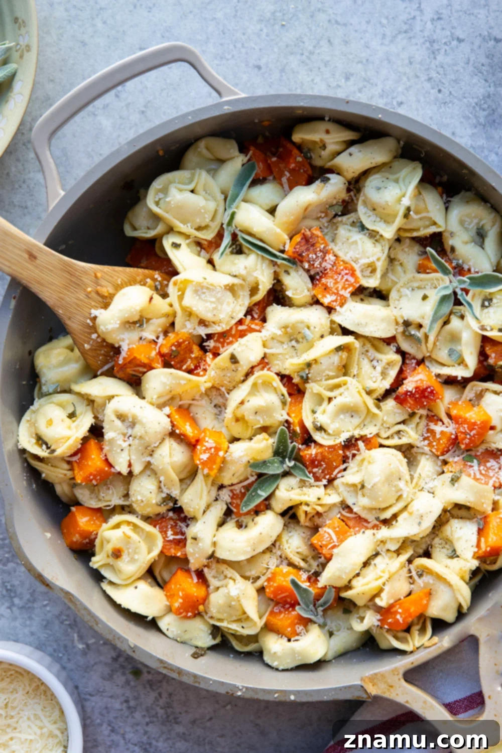 A large serving bowl filled with the finished butternut squash and tortellini, garnished with fresh sage and Parmesan.