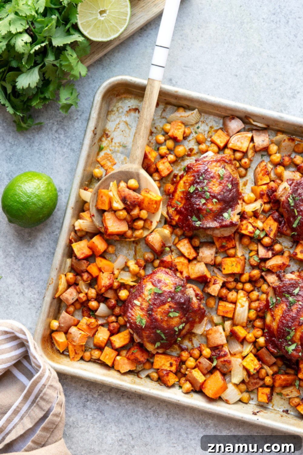 Sheet Pan Harissa Chicken with Roasted Sweet Potatoes & Chickpeas 2 Close-up of harissa chicken thighs with roasted sweet potatoes and chickpeas on a sheet pan, garnished with fresh cilantro.