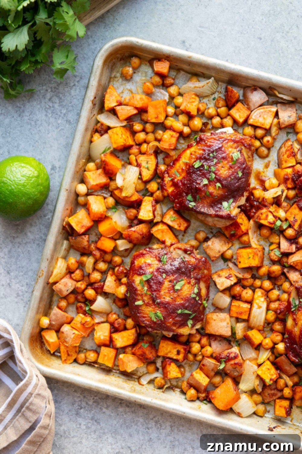 Sheet Pan Harissa Chicken with Roasted Sweet Potatoes & Chickpeas 4 Plated harissa chicken thigh with a side of roasted sweet potatoes and chickpeas, garnished with fresh cilantro.
