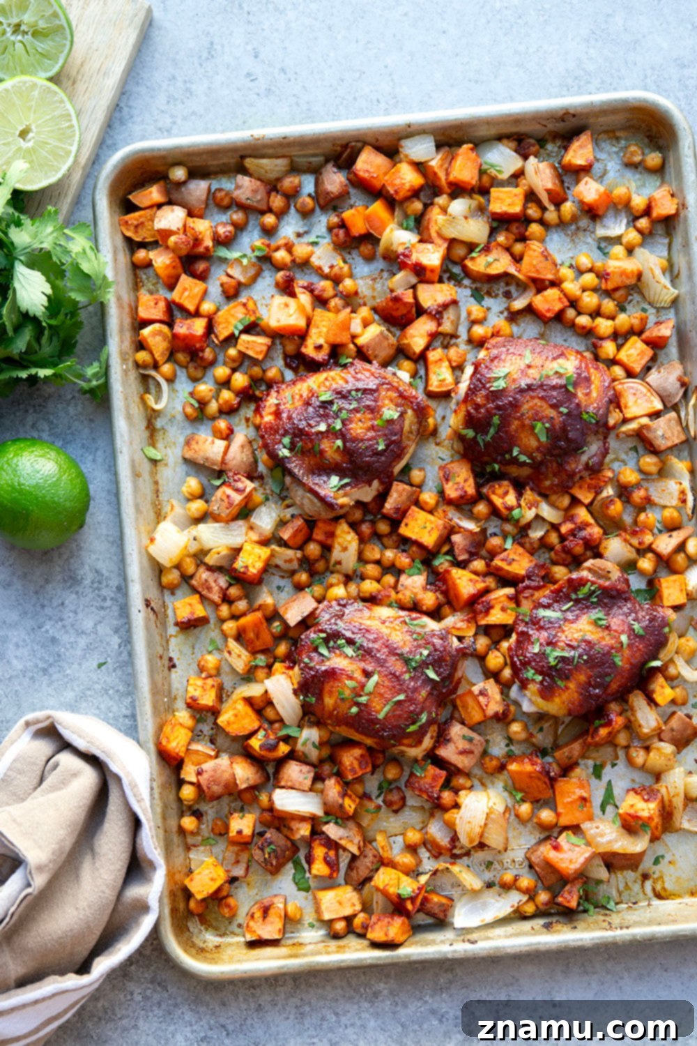 Sheet Pan Harissa Chicken with Roasted Sweet Potatoes & Chickpeas 6 A serving of harissa chicken and sweet potatoes, presented on a white plate with fresh lime and cilantro.