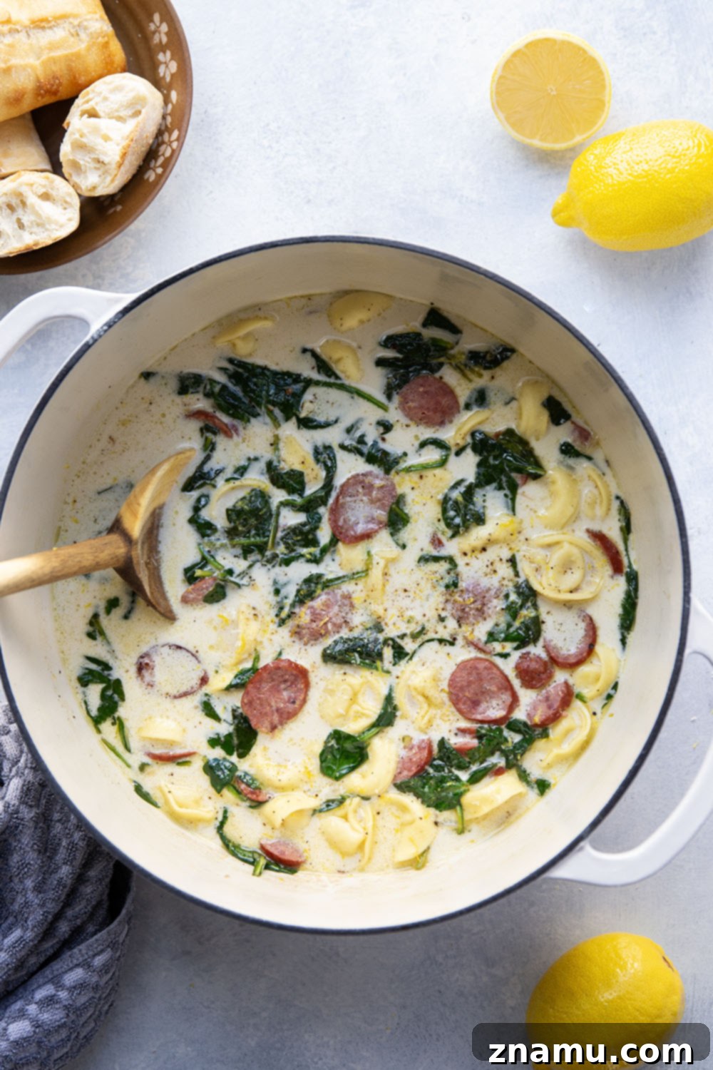 Sunshine Lemon Tortellini Soup 3 Close-up of a rustic bowl filled with creamy lemon tortellini soup, featuring visible pieces of sausage, spinach, and tortellini, with a spoon ready for tasting.