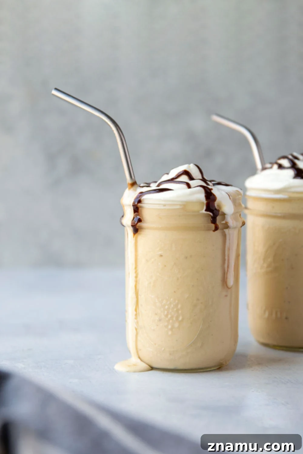 Peanut Butter Banana Blast 6 Two glasses of creamy peanut butter banana shakes, garnished with whipped cream and chocolate syrup, ready to be served.