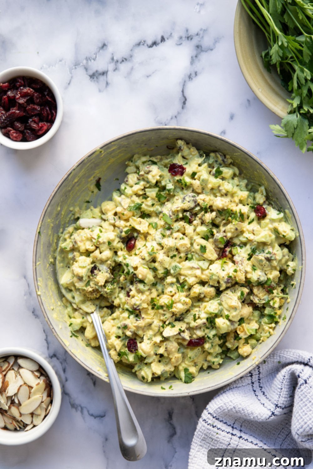 Sunshine Curried Chickpea Salad 2 A close-up shot of a vibrant curried chickpea salad with visible chickpeas, celery, almonds, and cranberries, garnished with fresh parsley.