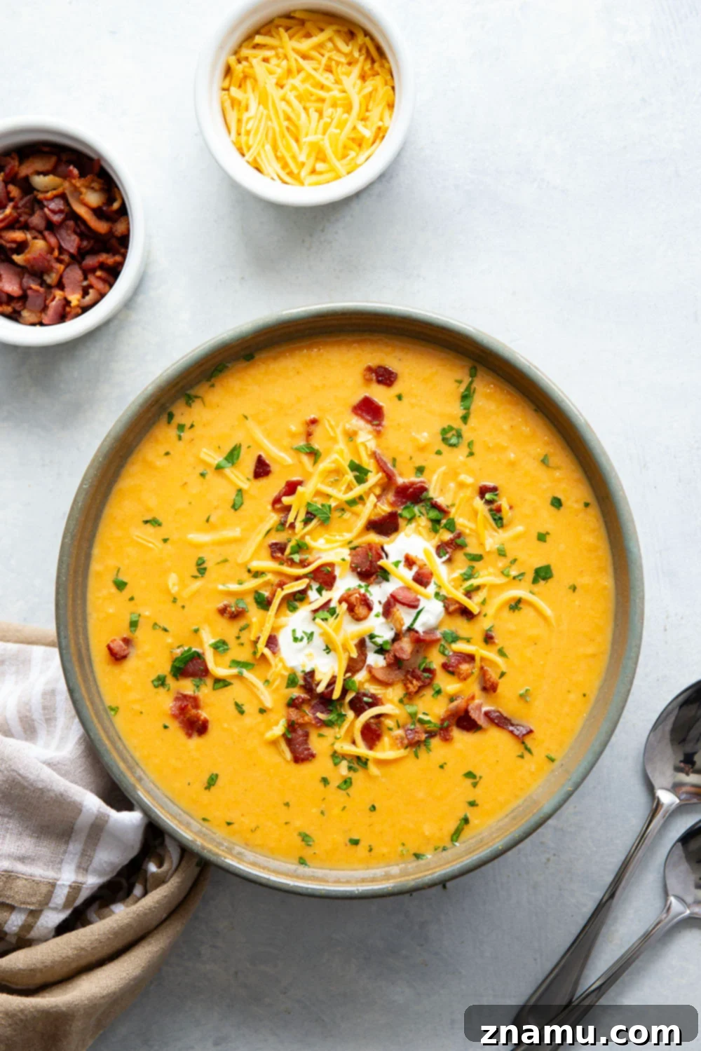 Ultimate Baked Sweet Potato Soup 2 A steaming bowl of creamy Loaded Baked Sweet Potato Soup, garnished with crispy bacon, shredded cheddar cheese, and a dollop of sour cream, ready to be enjoyed.