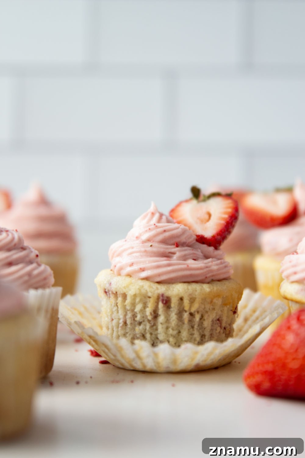 Strawberry Cream Cheese Cupcakes 3 Close-up of a single strawberry cupcake topped with swirls of pink cream cheese frosting and a fresh strawberry slice