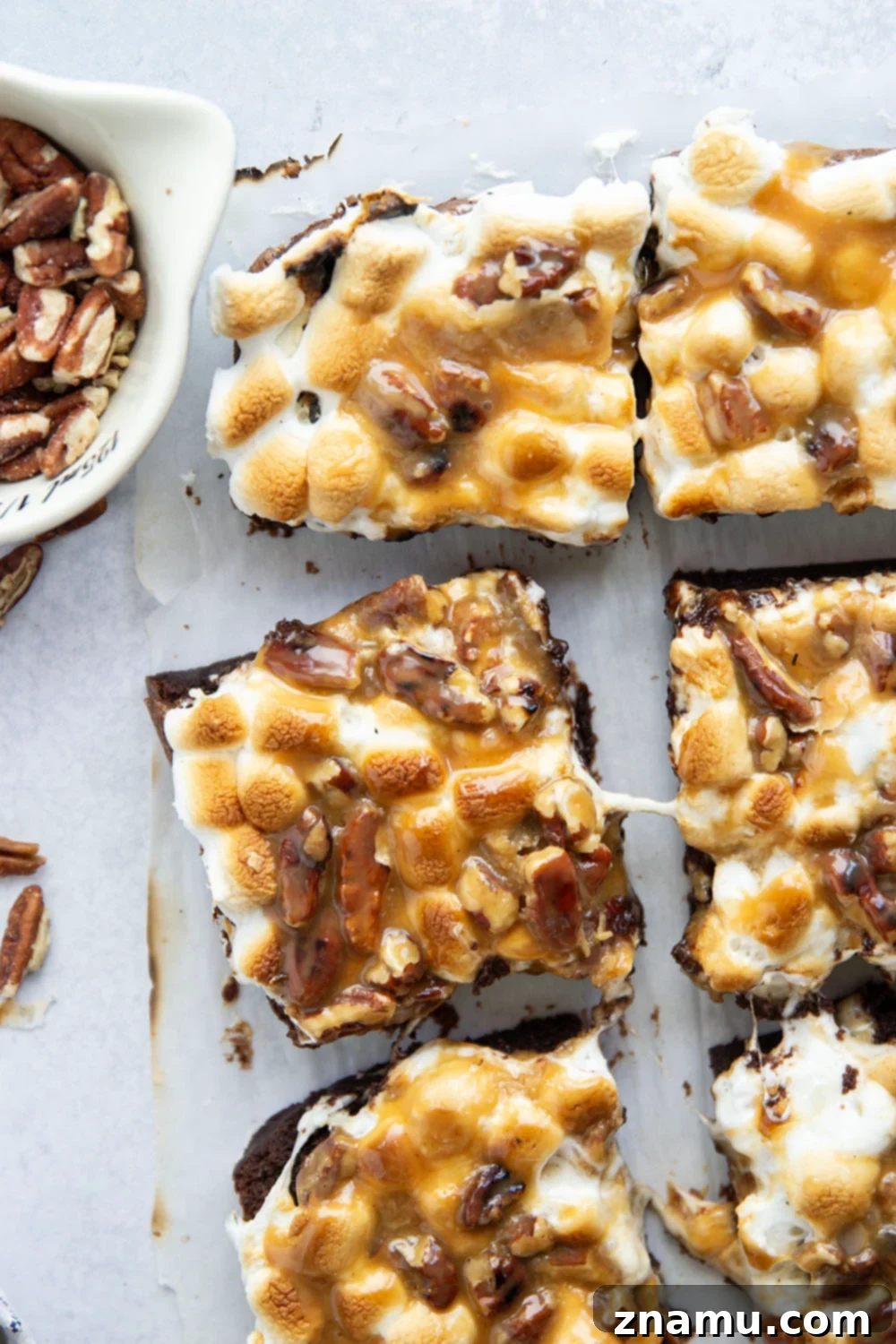 Stacked pieces of finished caramel pecan brownies, showing off their layers of fudgy chocolate, gooey marshmallow, and rich caramel.
