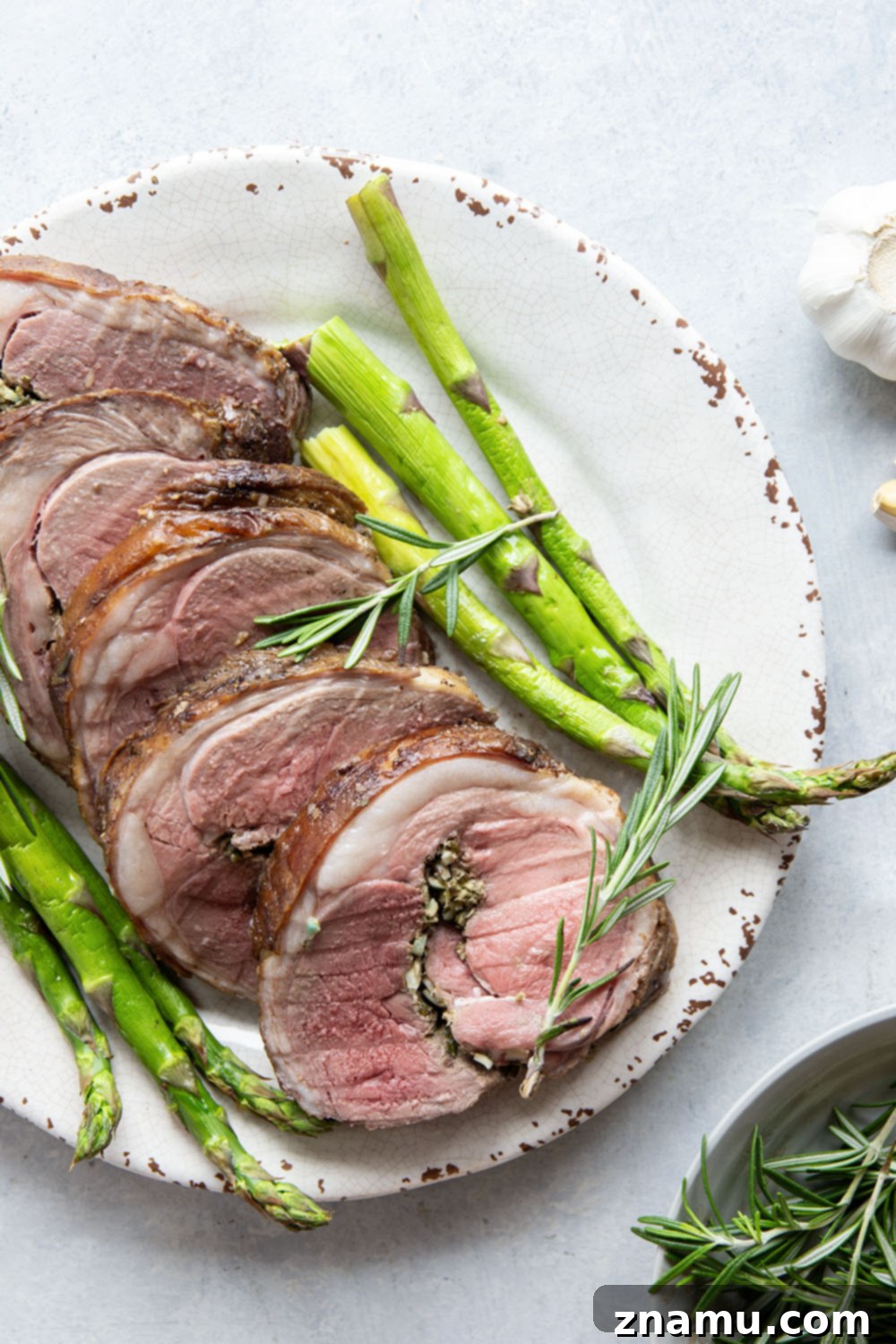 Aromatic Rosemary Garlic Leg of Lamb 6 Sliced rosemary garlic leg of lamb arranged beautifully on a serving platter with fresh herbs.