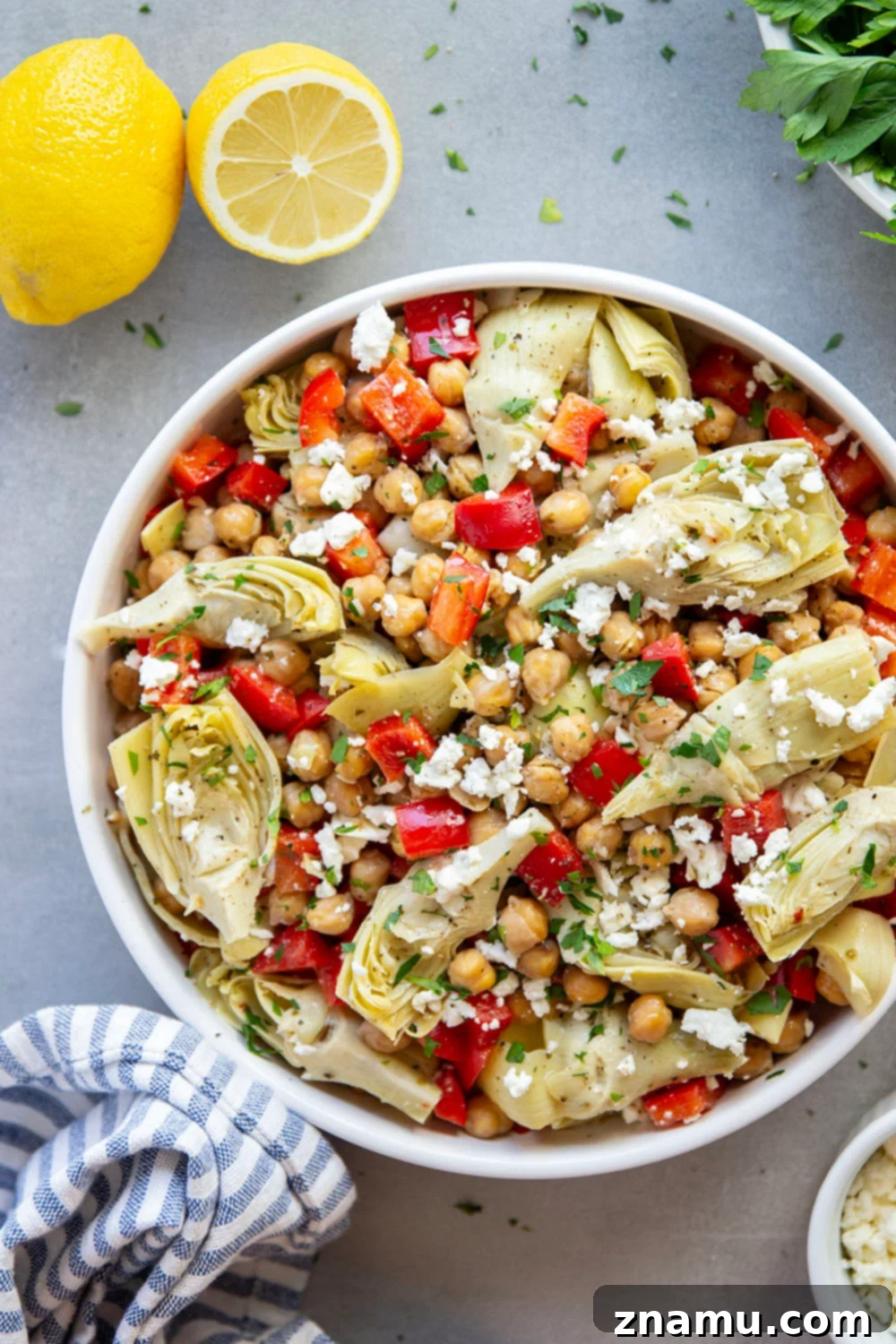 Zesty Artichoke and Crispy Chickpea Medley 3 Overhead view of a prepared Crispy Chickpea Artichoke Salad on a white plate, showing the colorful mix of chickpeas, artichokes, red bell pepper, and feta cheese, ready to be tossed with the lemon dressing. Ideal for healthy eating and meal prep.