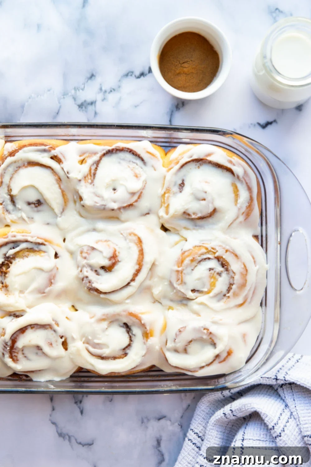 Wake Up To Warm Cinnamon Rolls 3 A pan of perfectly baked overnight cinnamon rolls, each one featuring a rich cinnamon swirl and a thick layer of white cream cheese frosting.