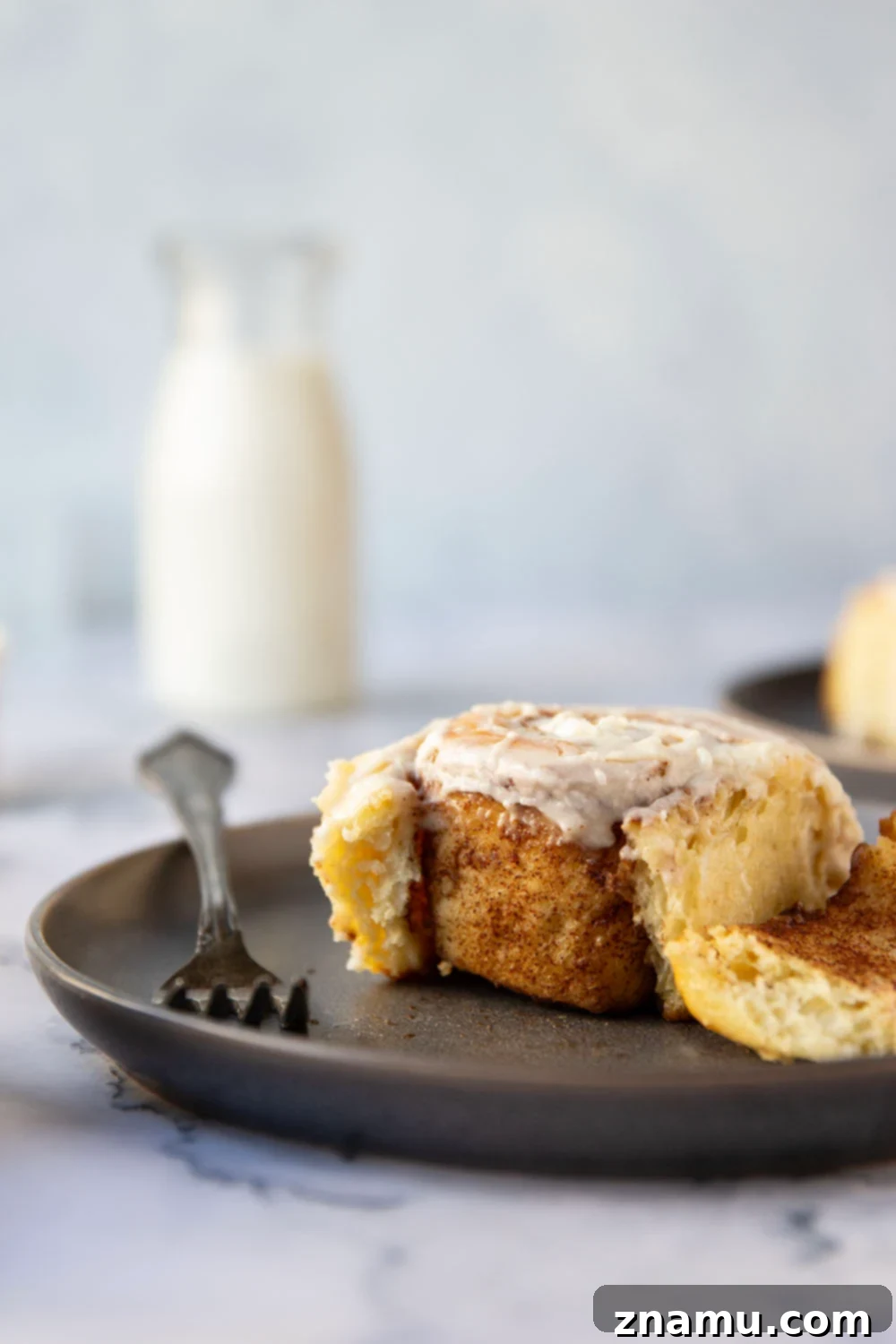 Wake Up To Warm Cinnamon Rolls 4 Close-up shot of an individual overnight cinnamon roll, showing the soft, golden-brown dough, the distinct cinnamon swirl, and the generous dollop of cream cheese frosting.