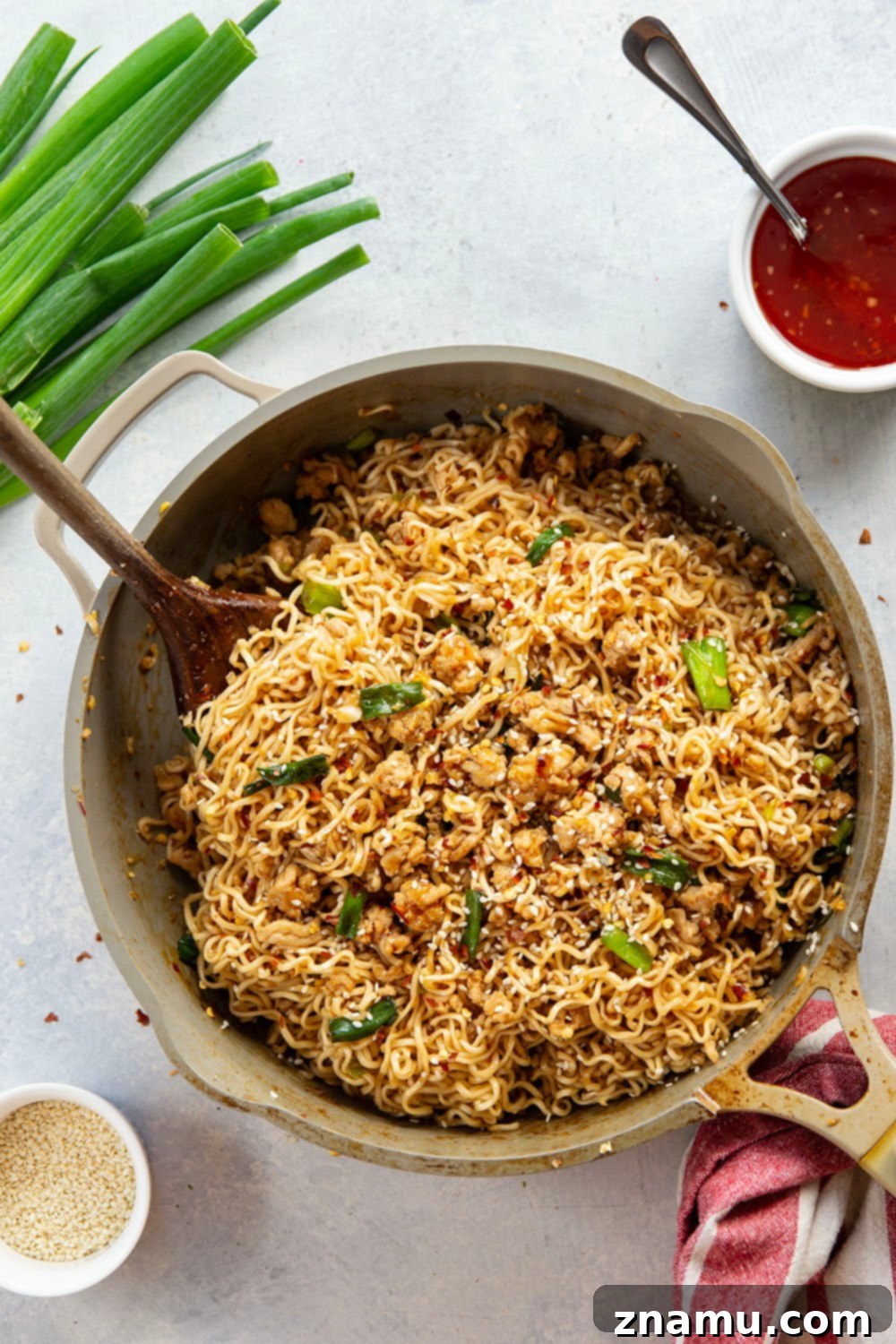 Sweet Chili Glazed Chicken Noodles 3 Overhead view of a wok filled with Ground Chicken Sweet Chili Noodles, showcasing the rich, glossy sauce clinging to every strand of noodle and piece of chicken, with fresh green onion garnishes.