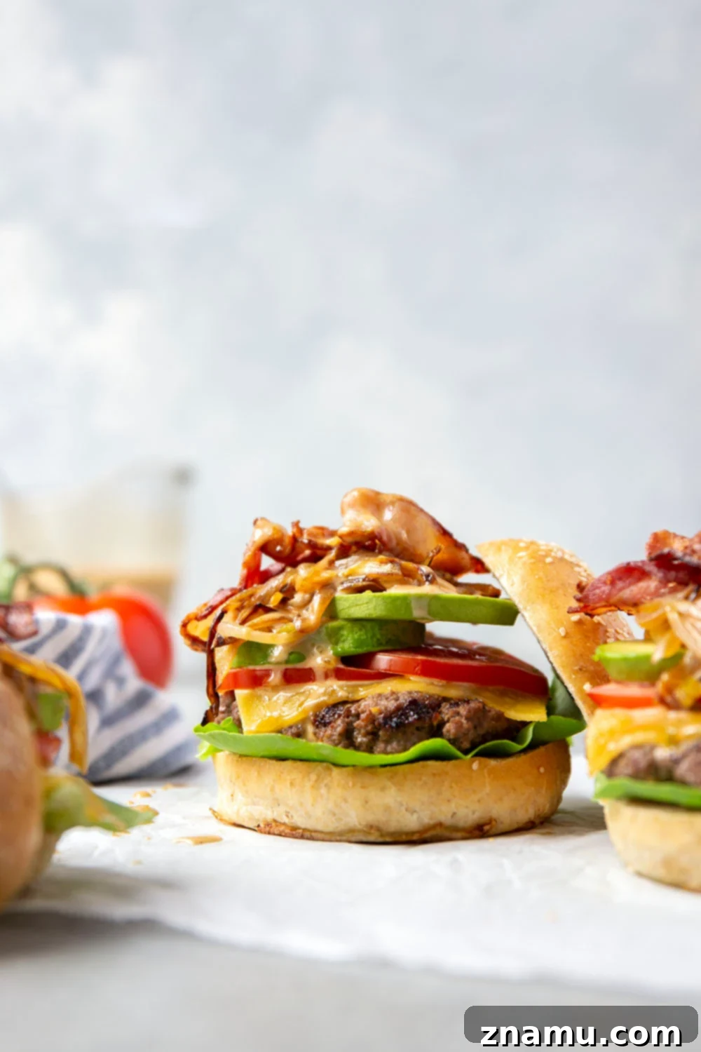 Hearty Cowboy Stack 2 Close-up of a stacked Loaded Cowboy Burger, showing a juicy patty, melted cheese, crispy bacon, caramelized onions, avocado, lettuce, and tomato on a toasted bun, drizzled with special sauce.