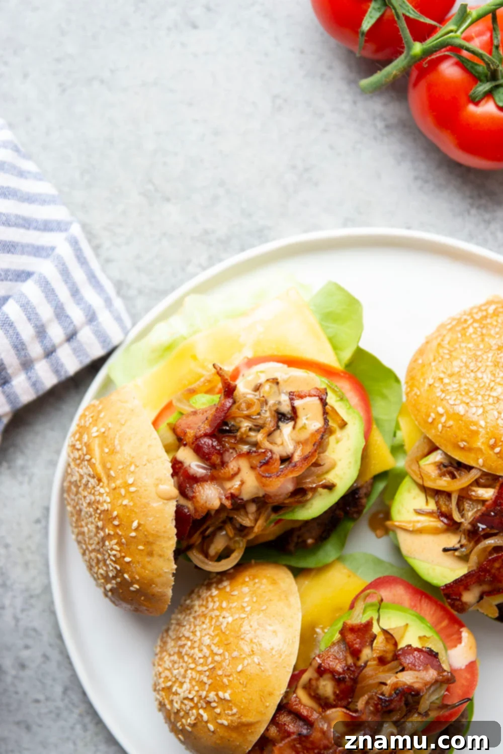 Hearty Cowboy Stack 3 Two fully assembled Loaded Cowboy Burgers on a wooden board, showcasing the various layers of ingredients including the grilled beef patty, melted cheese, bacon, avocado, and sauce.