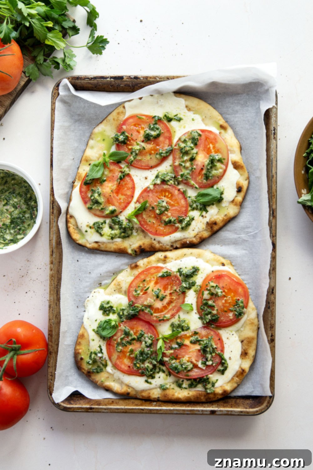 Fire-Kissed Caprese Flatbread with Aromatic Basil Chimichurri 3 Two grilled Caprese flatbreads on a cutting board, topped with basil chimichurri.