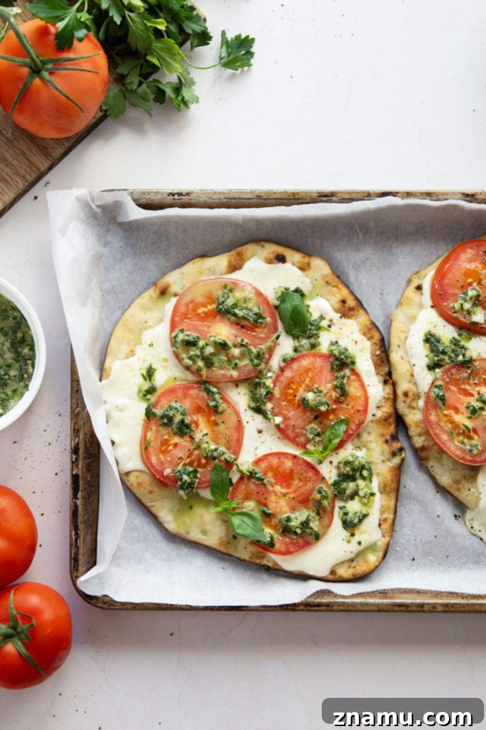 Fire-Kissed Caprese Flatbread with Aromatic Basil Chimichurri 5 A flatbread topped with slices of fresh mozzarella and red tomatoes, before grilling.