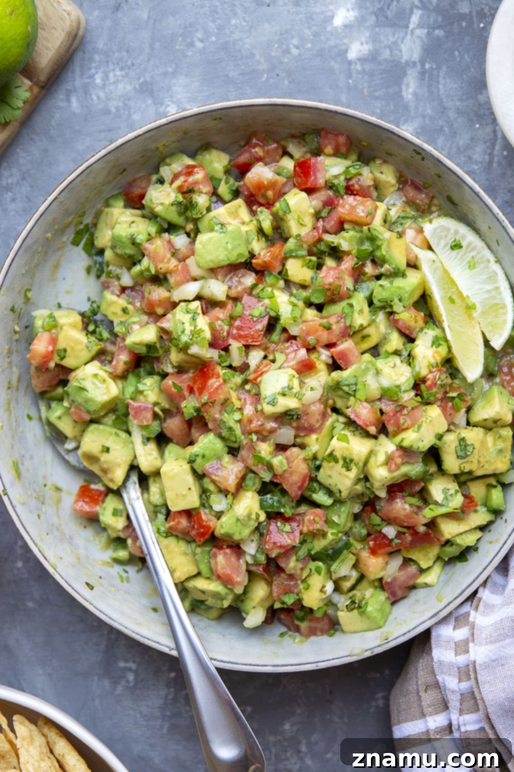 The Ultimate Chunky Avocado Salsa 6 A large serving bowl filled with chunky avocado salsa, garnished with extra cilantro and lime wedges, surrounded by a mountain of golden tortilla chips, inviting a group to share and enjoy.
