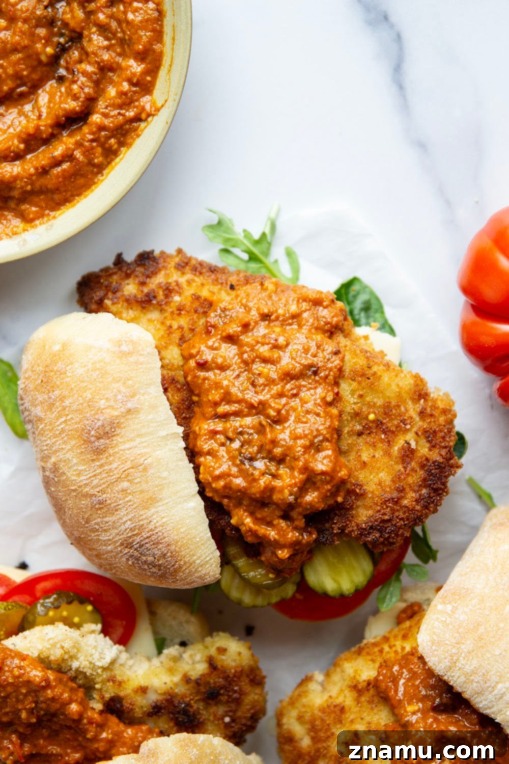 Romesco Chicken Crunch Sandwich 3 The components of a gourmet Crispy Chicken Romesco Sandwich laid out, including pan-fried chicken, homemade romesco, ciabatta, and fresh vegetables.