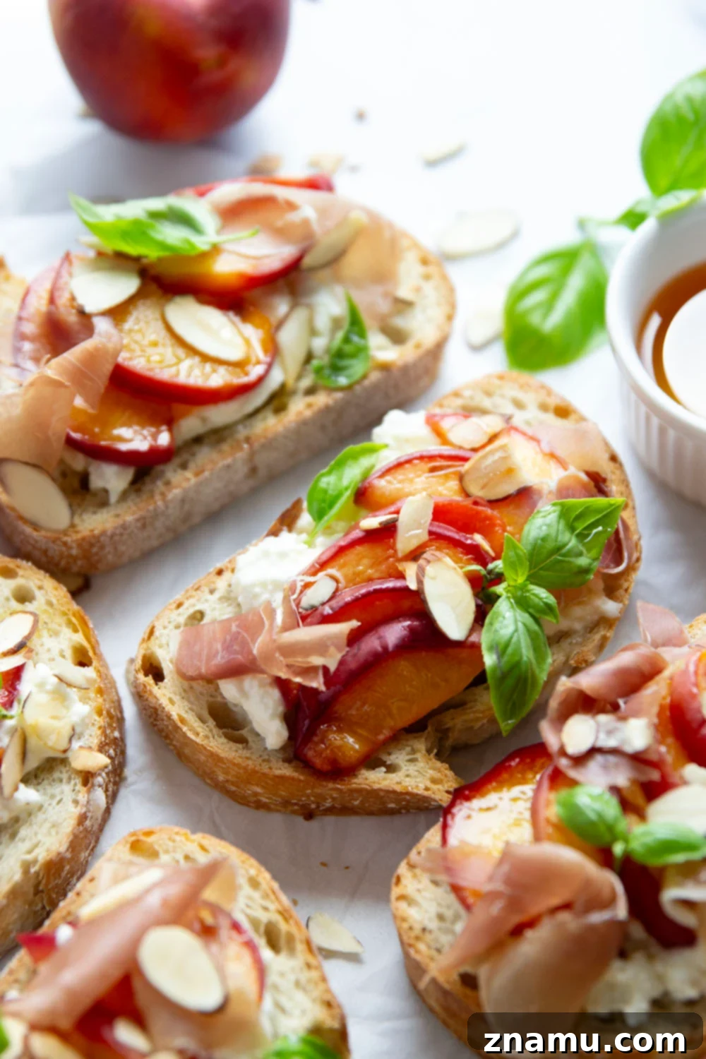 Burrata Toast with Honey Roasted Peaches 3 Close-up of a slice of Honey Roasted Peach Burrata Toast, garnished with basil and prosciutto.