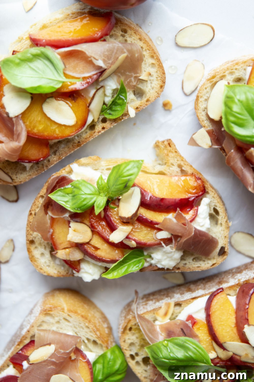 Burrata Toast with Honey Roasted Peaches 4 Ingredients for Honey Roasted Peach Burrata Toast laid out: peaches, honey, burrata, ciabatta, olive oil, basil, almonds, prosciutto.