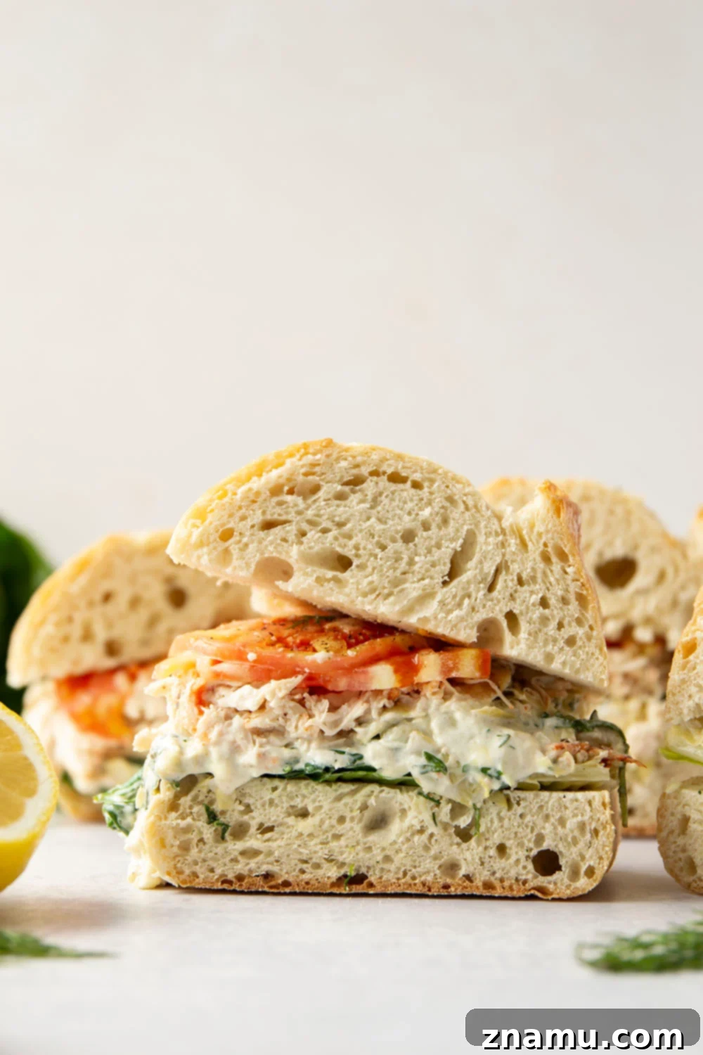 This gourmet spinach artichoke chicken sandwich features tender shredded chicken, creamy homemade spinach artichoke spread, and juicy tomato slices sandwiched between soft ciabatta bread.