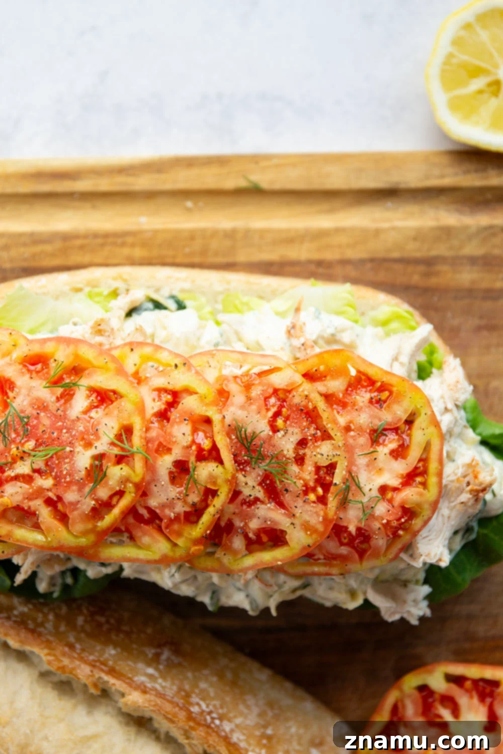 A close-up of a perfectly assembled spinach artichoke chicken sandwich on ciabatta bread, showcasing layers of creamy spread, chicken, and fresh tomato.