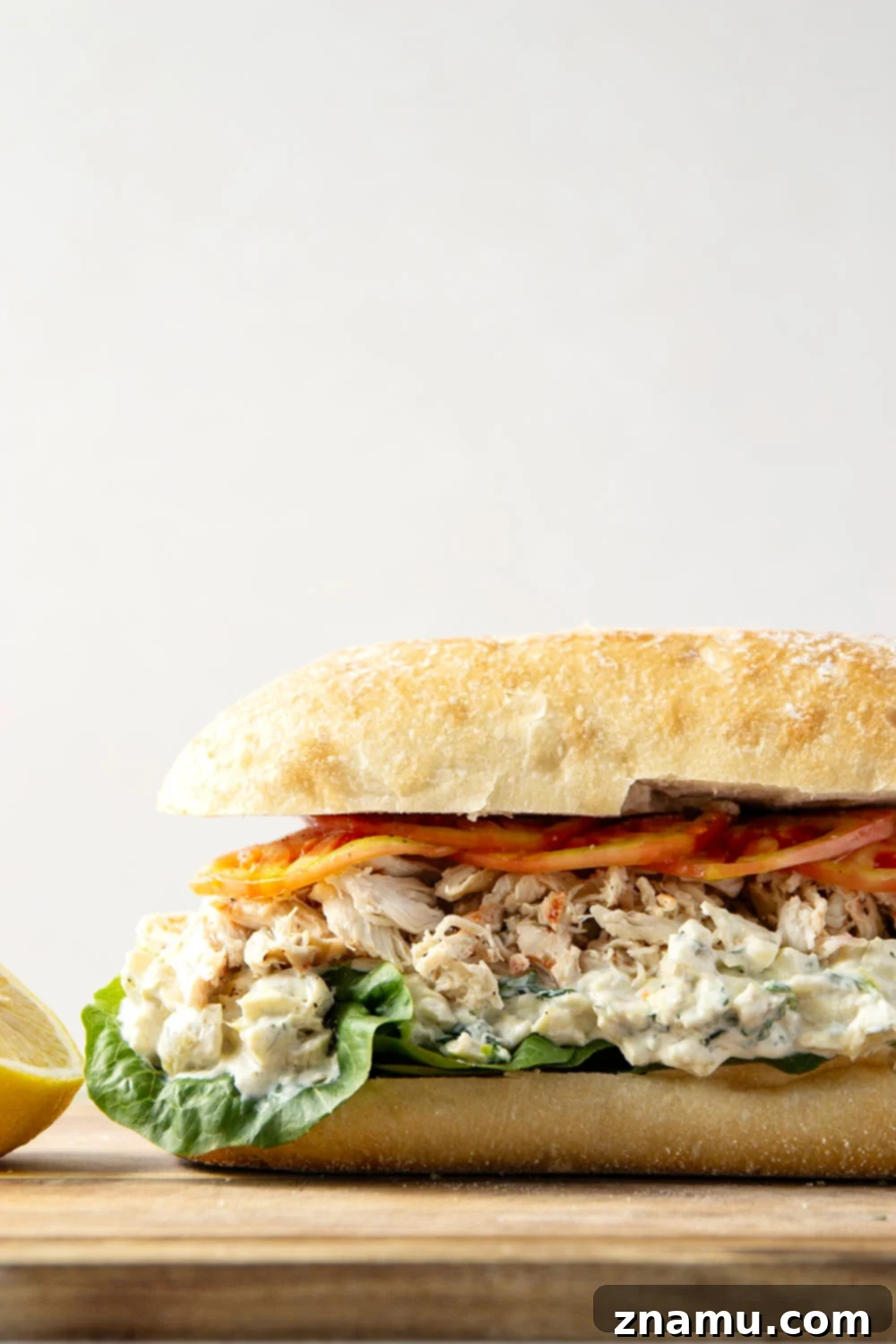 A side view of the spinach artichoke chicken sandwich, highlighting the thick layers and golden ciabatta bread.