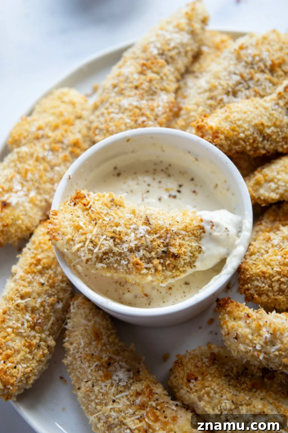 Plated oven-baked asiago chicken tenders with aioli and fresh herbs