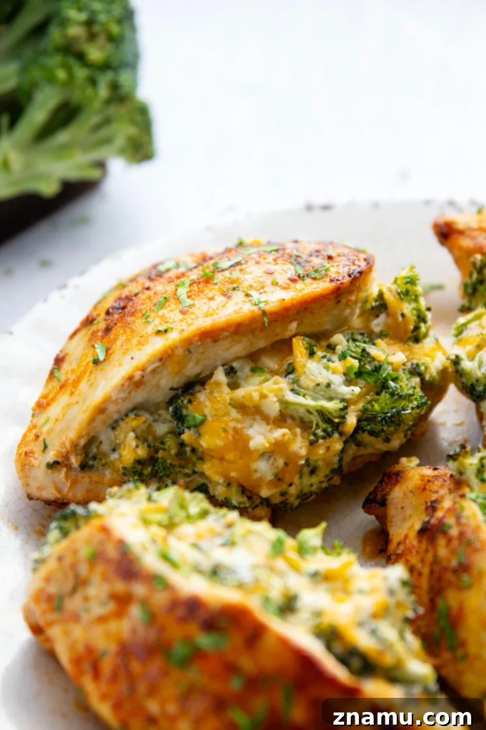 Broccoli and Cheese-Filled Chicken Breast 4 A plate featuring a golden-brown broccoli cheese stuffed chicken breast, garnished with fresh herbs, ready to be served.