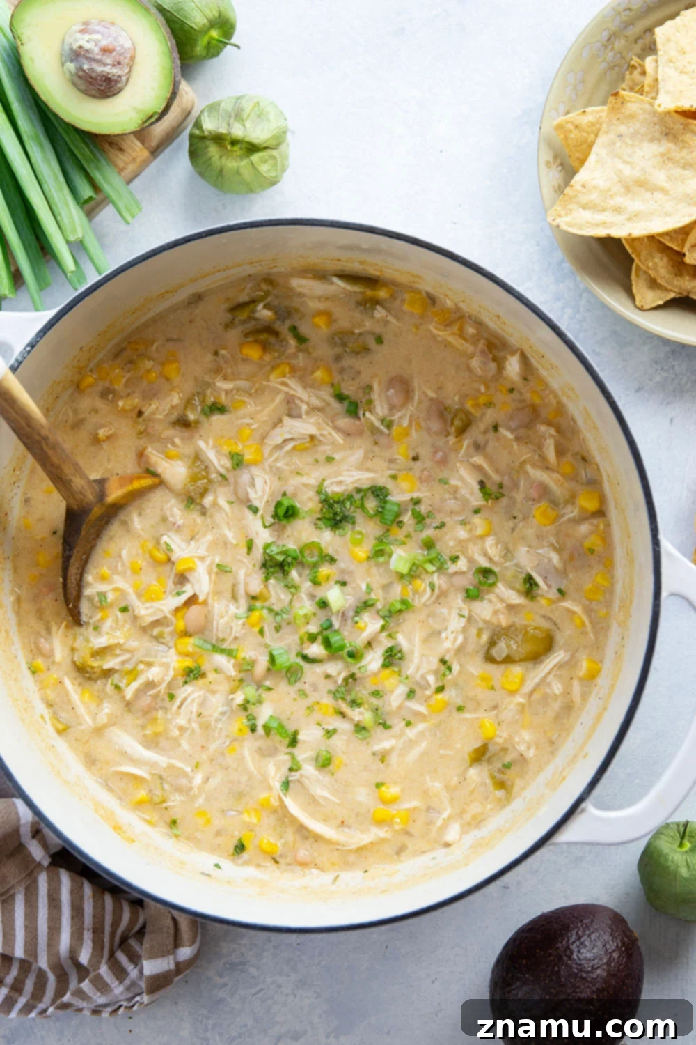 Smoky Verde Chicken Chili 6 A close-up of a steaming bowl of Tomatillo White Chicken Chili with a spoon, highlighting its creamy texture and rich toppings of cilantro and sour cream.